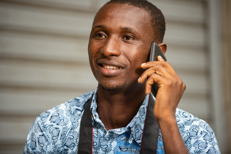 handsome young african photographer sitting outside holding a mobile phone and looking at camera...