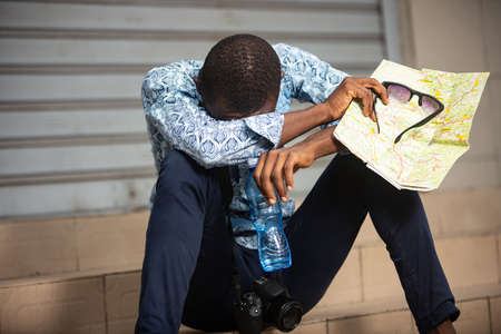 handsome young african photographer sitting outside holding a mobile phone and looking at camera smilingの写真素材