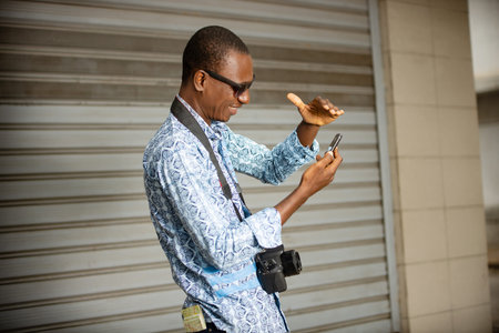 young tourist standing in farcloth shirt outdoors communicating with mobile phone with camera neck.