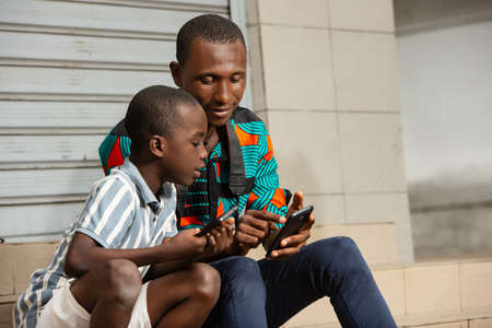 handsome young father sitting with his son, father showing images to his son on mobile phone in the street while smilingの写真素材