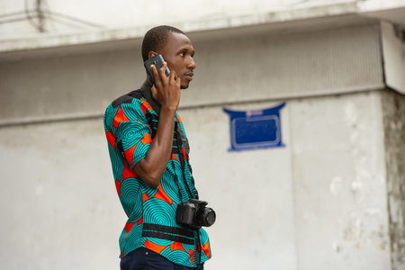 young tourist standing in farcloth shirt outdoors communicating with mobile phone with camera neck.の写真素材