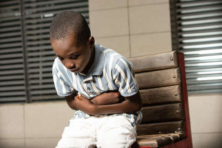 pretty little african boy sitting on a bench and suffering from strong stomach painの写真素材