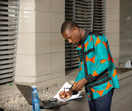 Businessman is standing in front of a computer, looking at the mobile phone, and records informationの写真素材