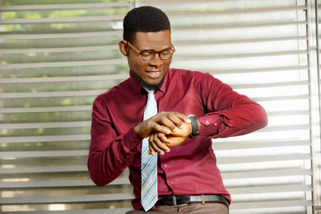 handsome adult businessman standing near the desk and looking at the time on his watch smilingの写真素材