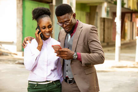 young beautiful african couple standing using a mobile phone while smiling on the streetの写真素材