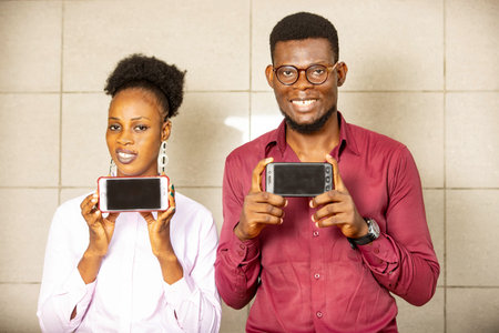 Two students stand together and hold their phones in their hands. Looking at the camera and smiling....