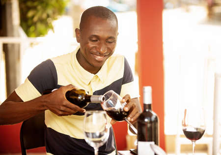 handsome young man sitting near a bar serving and drinking a glass of red wineの写真素材