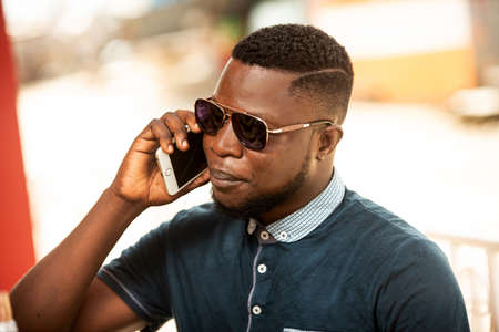 Successful young african man candidate having a conversation on his smartphone during work break sitting outside the building. Experienced CEO talking with a cell phone, outside against a companyの写真素材