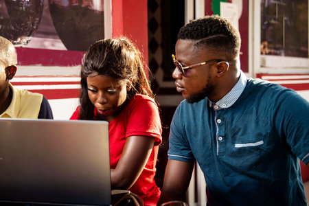 portrait of young students sitting on a restaurant table and working using a laptop computer while...