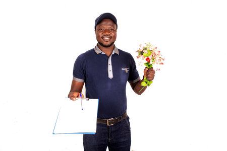 young delivery man in cap standing on white background holding bouquet of flowers box and note pad smiling.の写真素材
