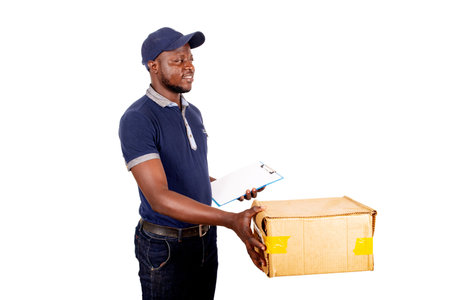 young delivery man in cap standing on white background holding note pad and cardboard box smiling.