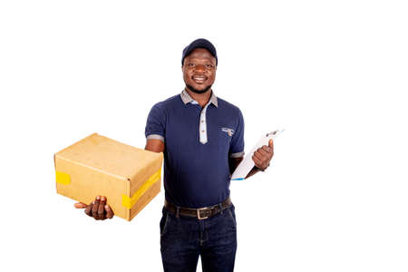 young delivery man in cap standing on white background carrying cardboard box and note pad smiling.の写真素材