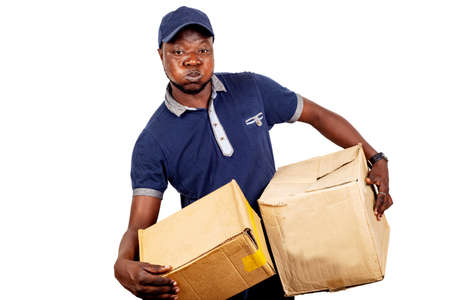 young delivery man standing in hat on white background carrying boxes in very heavy boxes.の写真素材