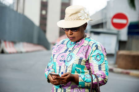 beautiful adult businesswoman wearing glasses and a Belgian hat walking with a mobile phone in the streetの写真素材