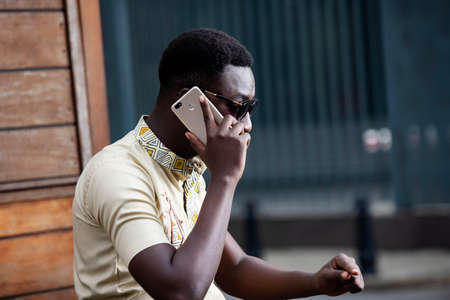 handsome young man wearing sunglasses sitting sideways outdoors and talking on mobile phoneの写真素材