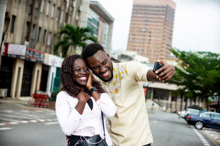 young couple standing outdoors photographing themselves smiling.の写真素材