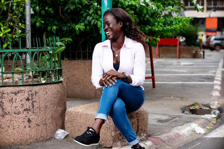 beautiful young african woman sitting in the street and smilingの写真素材