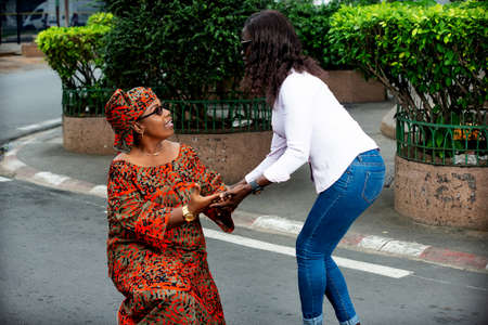benevolent beautiful woman in shirt helping woman in red loincloth rising in the streetの写真素材