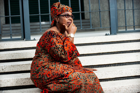 beautiful mature woman wearing glasses sitting on stairs outdoors in the street and thinking and regrading highの写真素材