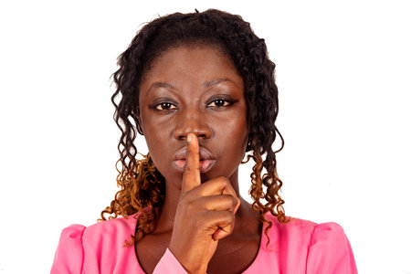 serious, beautiful young woman making a gesture of silence with the finger on the lips and looking...