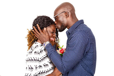 young man in glasses standing on white background giving kiss on the forehead of his girlfriend holding a flower laughingの写真素材