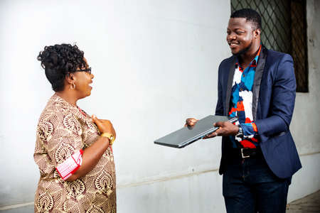 happy businessman offering a laptop has a woman indoors while being smilingの写真素材