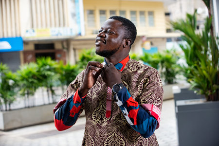 handsome young businessman standing and looking sideways buttoning his shirt outdoors in the street...