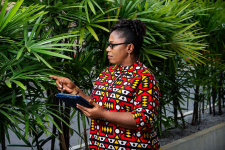 happy beautiful adult woman in eyeglasses using a digital tablet pointing with hand and finger on the side in the streetの写真素材