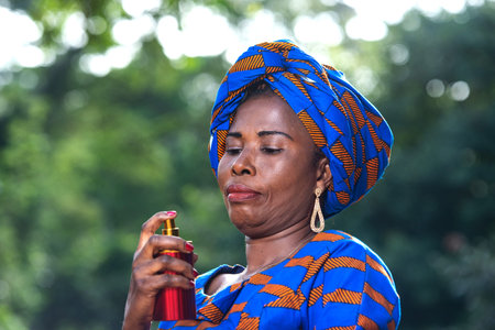 beautiful adult businesswoman standing and applying a bottle of red perfume in the park.