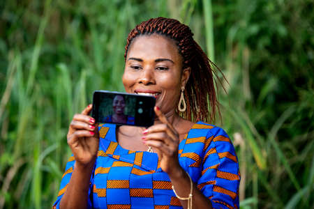 beautiful adult woman standing in the park and taking picture using a mobile phone smiling.の写真素材