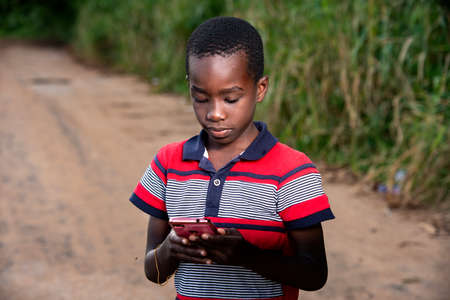 a young boy in t-shirt standing in the countryside looking at mobile phone.の写真素材