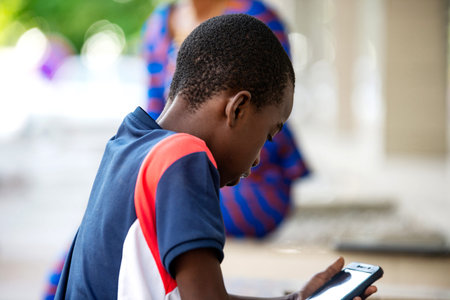 handsome little boy standing outdoors using a mobile phone and looking at the touch screen.