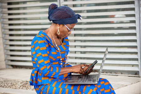 beautiful adult businesswoman sitting outside using a mobile phone with a laptop.の写真素材