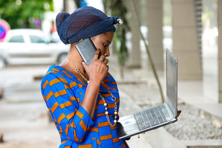 beautiful mature businesswoman in traditional outfit standing outdoors communicating to mobile phone...