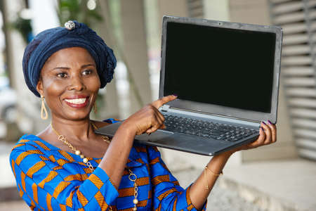 beautiful mature businesswoman in traditional outfit standing outdoors showing a laptop and looking at the camera smiling.の写真素材