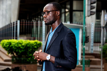 handsome serious adult businessman wearing glasses with jacket standing aside on the street with crossed hands.の写真素材