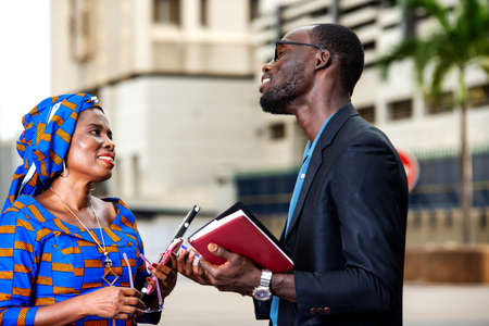 businessman and businesswoman talking about business standing on the street with each a notebook in hand.の写真素材