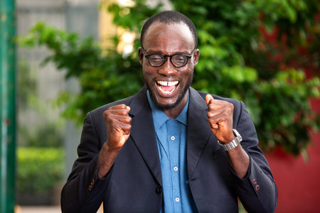 handsome businessman in suit standing outdoors screaming of joy with closed fists.