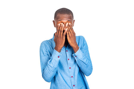 adult businessman wearing a blue shirt hiding his eyes with his hands.