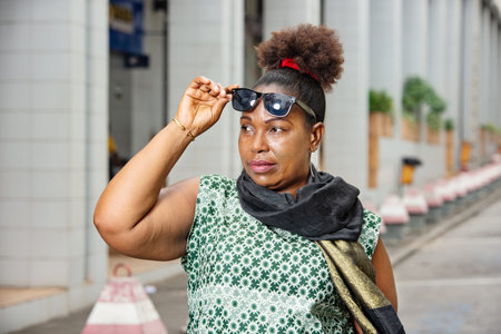 a beautiful mature woman in a dress with sunglasses and escapes standing outdoors looking away