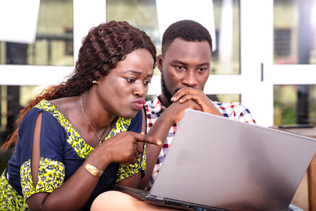 Serious adult business people sitting on chairs and working on laptop together. woman pointing...
