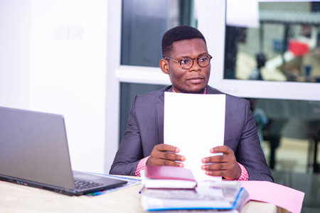 Serious adult businessman sitting in front of laptop and holding paper report in office.の写真素材