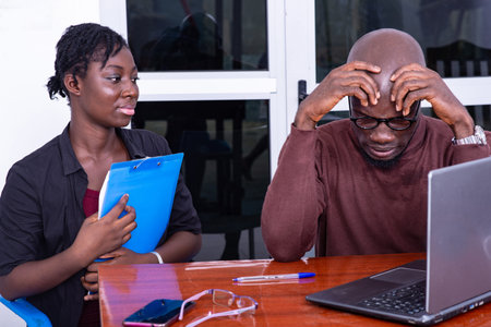 Businessman and woman sitting at table in meeting room with open laptop and chatting. man suffering...