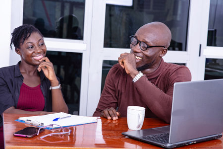 Businessman and woman sitting at table in meeting room with open laptop and while discussing.