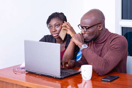 two serious business partners sitting at the desk and working together on laptop. woman talking on mobile phone.のeditorial素材