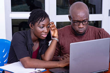 two serious business partners sitting at the desk and working together on laptop. woman talking on mobile phone.のeditorial素材