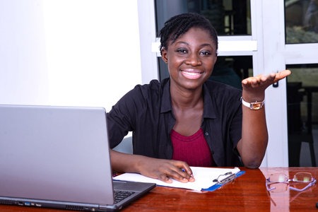 young serious businesswoman sitting at the desk and working, smiling at the camera.