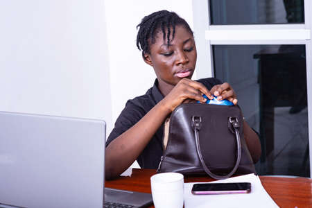 young businesswoman sitting at the desk taking something from her purseの写真素材