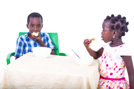 cute little kids having breakfast while eating bread at the table at home.の写真素材