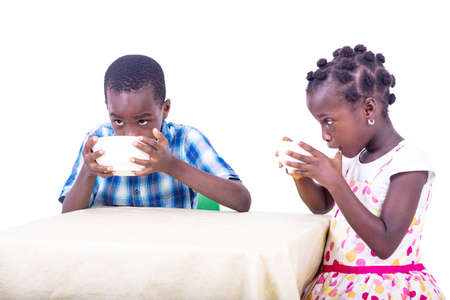 two cute little children sitting at the table having breakfast while drinking milk at home.の写真素材